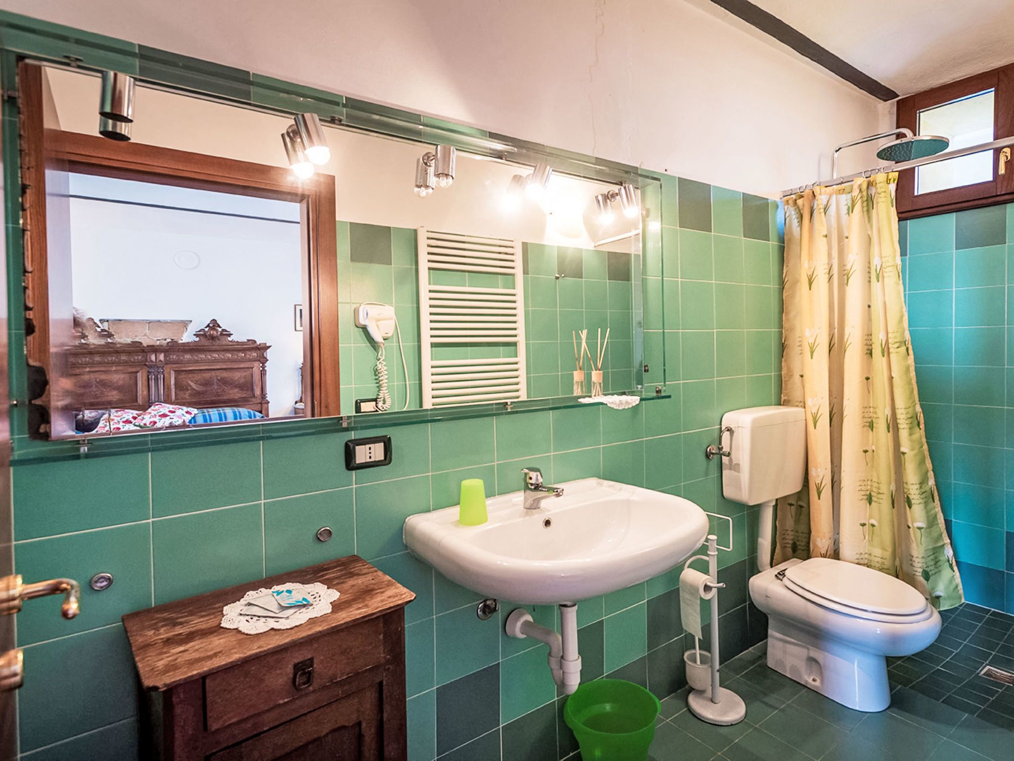 Een badkamer met groene tegels, een wastafel, een toilet, een spiegel en een houten wastafelmeubel.