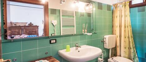 Een badkamer met groene tegels, een wastafel, een toilet, een spiegel en een houten wastafelmeubel.