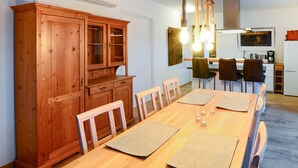Een eetruimte met een houten tafel en stoelen, een houten kast en een keuken op de achtergrond.
