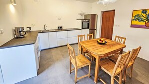 Et moderne køkken med en central ø, et spisebord med stole og en hængende lampe.