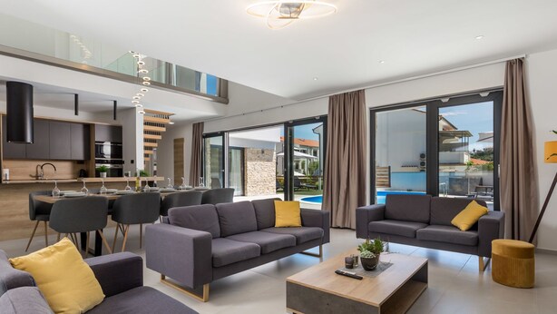 A modern living room with grey sofas, a wooden coffee table, and a dining area with a glass top table. - Pinnidae by Interhome (Rab/Lopar)