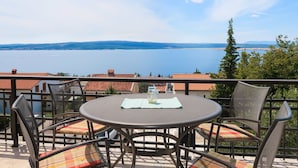 Eine Terrasse mit einem runden Tisch und Stühlen, mit Blick auf ein Gewässer und Hügel in der Ferne.