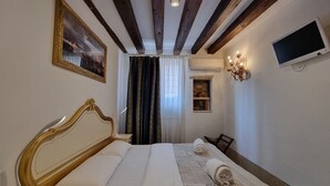 A hotel room with a large bed, a TV mounted on the wall, and a small window with curtains. - Gesuiti Cozy and Central Apartment by Ca-sa Check (Venice)