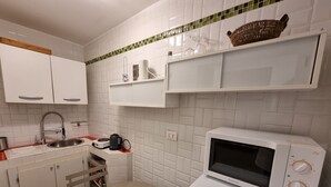 A compact kitchen with white cabinets, a microwave, a kettle, and a small table. - Gesuiti Cozy and Central Apartment by Ca-sa Check (Venice)