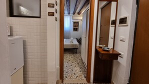 A narrow hallway with a washing machine, a bed with a white bedspread, and a mirror on the right. - Gesuiti Cozy and Central Apartment by Ca-sa Check (Venice)