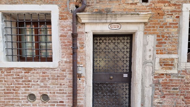A brick building with a metal gate and a window with bars. - Gesuiti Cozy and Central Apartment by Ca-sa Check (Venice)