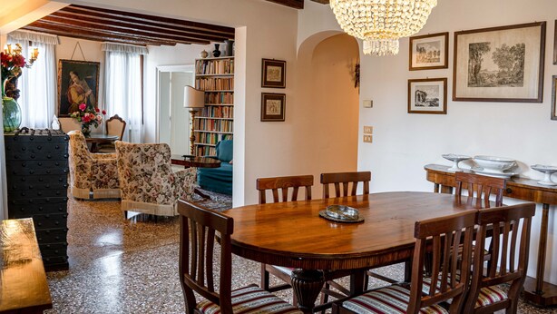 A dining area with a wooden table and chairs, a chandelier, and a bookshelf in the background. - Casa Allegra by Ca-sa Check (Venice)