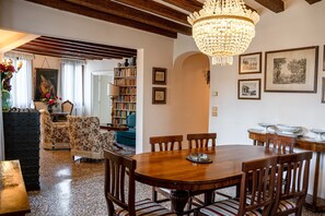 A dining area with a wooden table and chairs, a chandelier, and a bookshelf in the background. - Casa Allegra by Ca-sa Check (Venice)