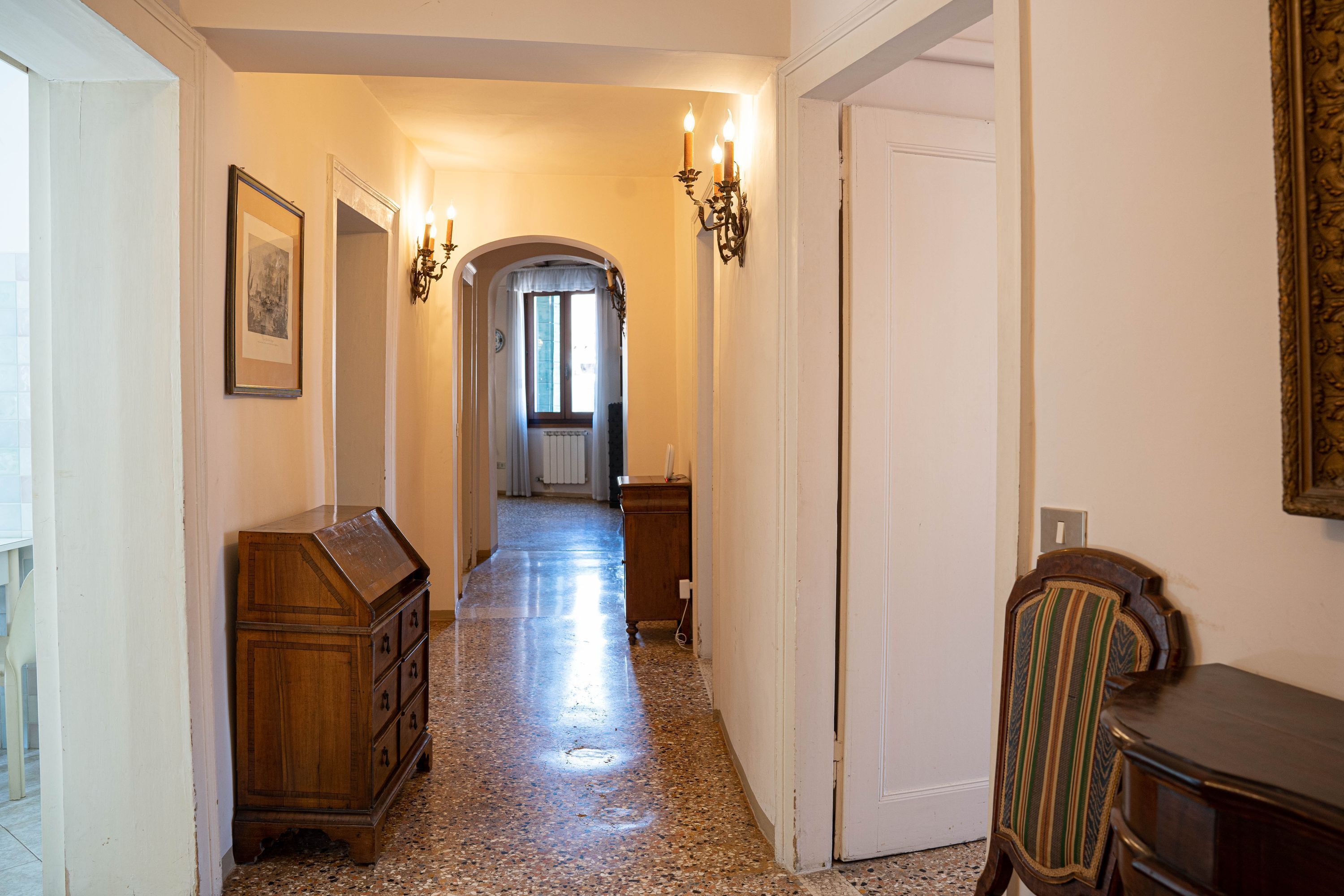 A hallway with a wooden dresser, a chair, and a door leading to another room.