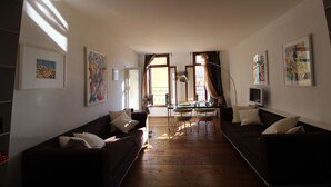 A living room with a dark brown sofa, a glass coffee table, and a TV on a stand. There are two windows with curtains, and artwork on the walls. - Apartment in the Heart of Venice by Ca-sa Check (Venice)