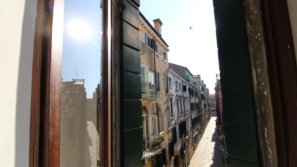 A narrow street with buildings on either side, a clear sky, and a person walking down the street. - Apartment in the Heart of Venice by Ca-sa Check (Venice)