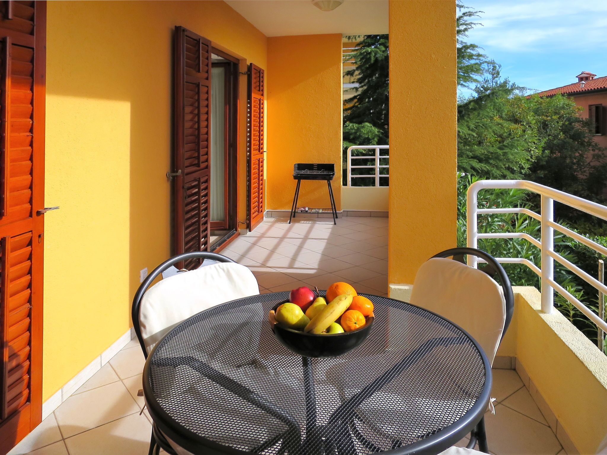 A balcony with a round table, chairs, and a bowl of fruit.