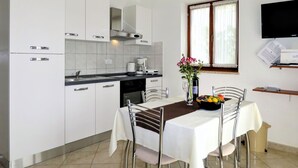 Une cuisine moderne avec des meubles blancs, une table à manger recouverte d’une nappe blanche et une fenêtre avec des rideaux.