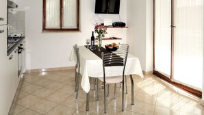 Un coin repas avec une table dressée pour deux personnes, un téléviseur fixé au mur et une fenêtre avec des rideaux.
