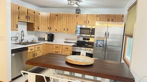 A kitchen with wooden cabinets, stainless steel appliances, and a central island with chairs. - Pleasant Mountain Escape 5BR Condo with Moose Pond Access (Bridgton)