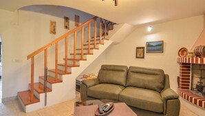 A living room with a wooden staircase, a green sofa, a coffee table with a remote control, and a fireplace.