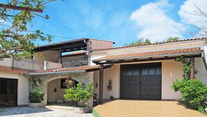 A two-story building with a stone archway entrance, a tiled patio, and a balcony with a railing.