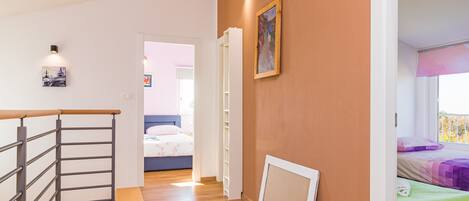 A room with a wooden floor, a bed with a green bedspread, a white door, and a painting on the wall.