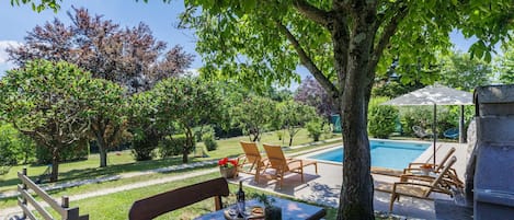A poolside area with a table and chairs, a stone structure, and a view of a swimming pool.