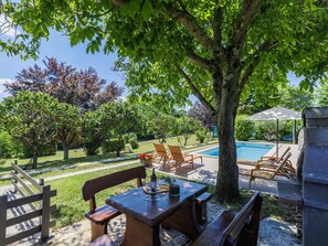 A poolside area with a table and chairs, a stone structure, and a view of a swimming pool.
