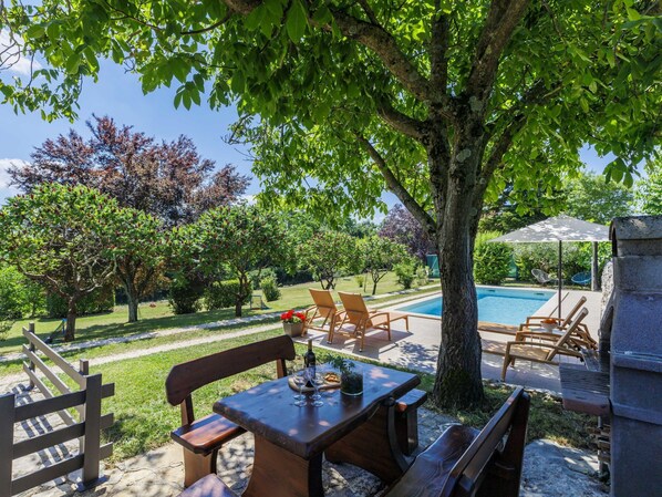 A poolside area with a table and chairs, a stone structure, and a view of a swimming pool.