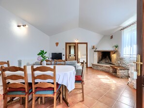 A dining area with wooden chairs and a table, a living room with a sofa and TV, and a stone fireplace.