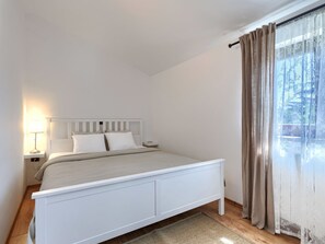 A bedroom with a bed, a nightstand, a lamp, and a window with curtains.