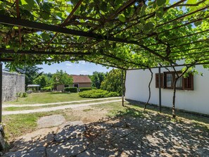 A stone pathway leading to a white building with a tiled roof, surrounded by greenery and a clear sky.