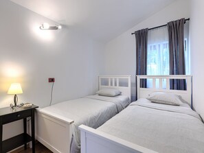 A bedroom with two beds, a bedside table with a lamp, and a window with curtains.