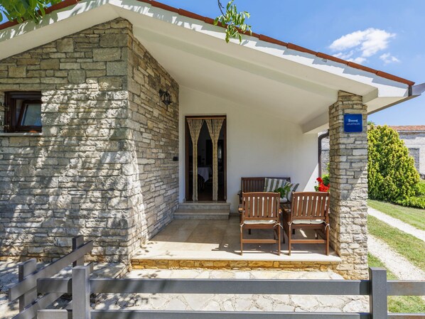 A stone building with a covered porch, a wooden chair, a small table, and a sign indicating it's an apartment.