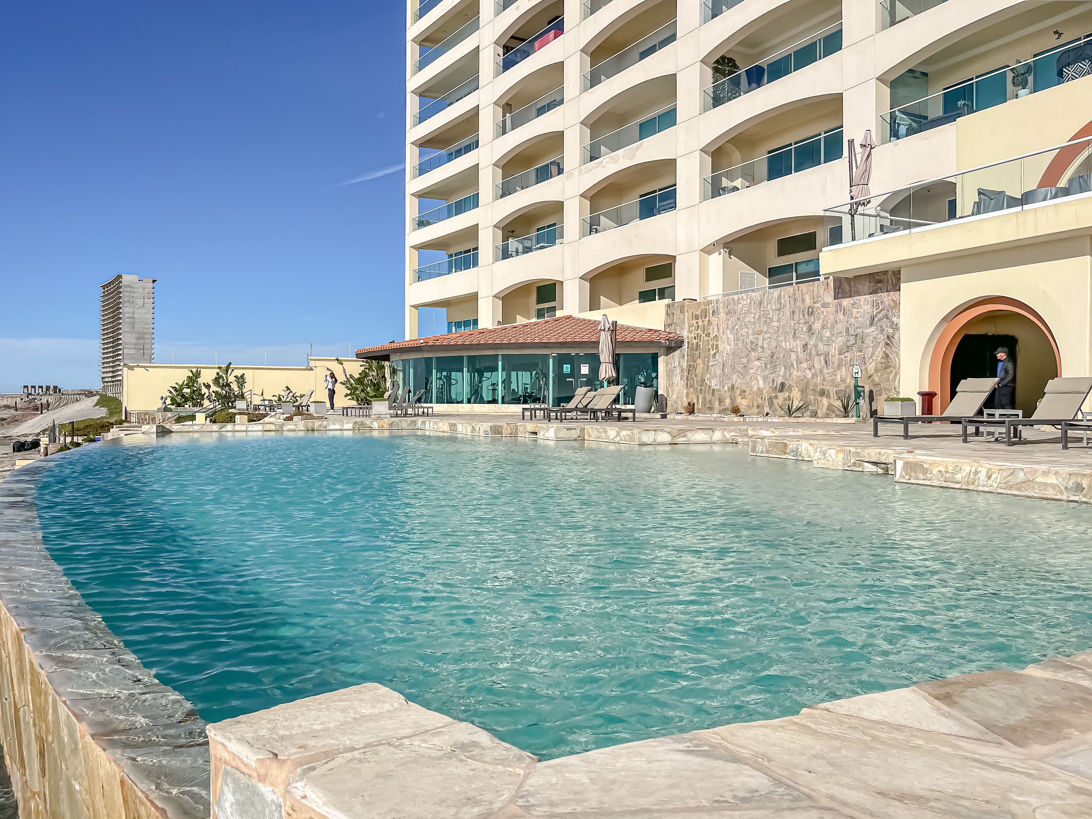 A hotel with a swimming pool, multiple balconies, and a view of the surrounding area.