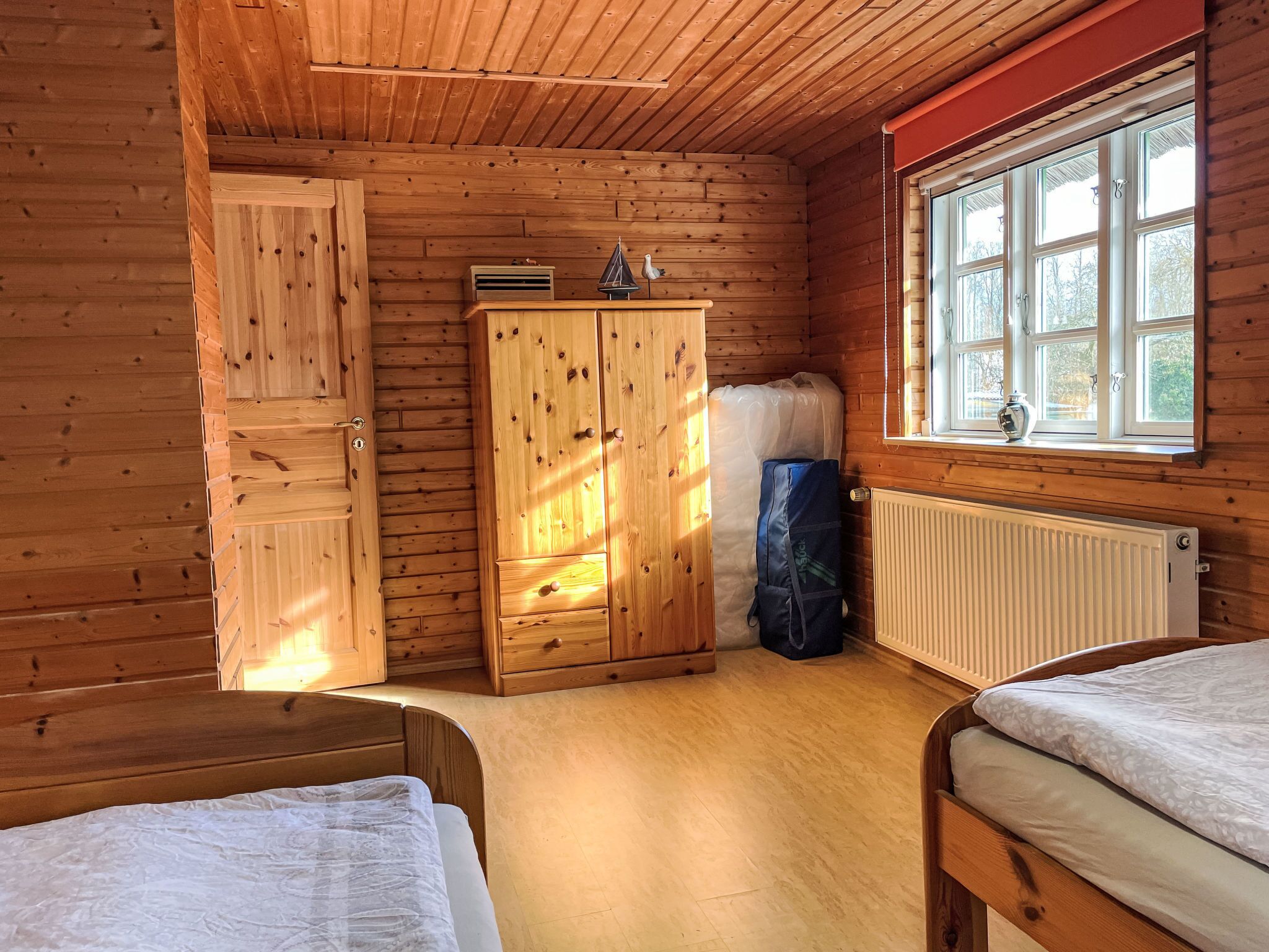 A wooden cabin room with a bed, a wardrobe, a radiator, and a window.