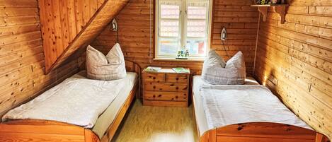 A cozy cabin room with two wooden beds, a small dresser, and a window with a view.