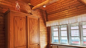 A wooden cabin room with a bed, a large wardrobe, and a window with curtains. - Brigitte by Interhome (Katzow)
