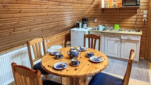 A cozy wooden cabin with a dining area featuring a round wooden table set with plates, cups, and a teapot. There is a kitchen area with a microwave, sink, and cabinets. - Brigitte by Interhome (Katzow)