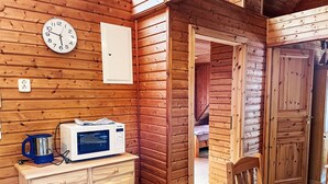 A wooden cabin interior with a microwave on a counter, a clock on the wall, and a door leading to another room. - Brigitte by Interhome (Katzow)
