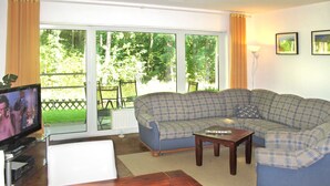 Ein Wohnzimmer mit einem blau karierten Sofa, einem Holztisch und einem Fernseher auf einem Lowboard.
