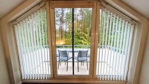Una habitación con un gran ventanal corredera que da a un patio exterior con dos sillas y una mesa.