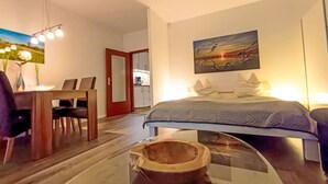 Una habitación de hotel moderna con cama, una mesa de comedor con sillas, una zona de cocina y un cuadro en la pared.