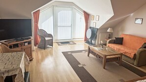 Een ruime woonkamer met een grote televisie, comfortabele zithoek en uitzicht op het landschap door een groot raam.