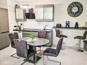 Cozinha moderna com mesa de jantar redonda, cadeiras estofadas em cinza, forno embutido e máquina de café.