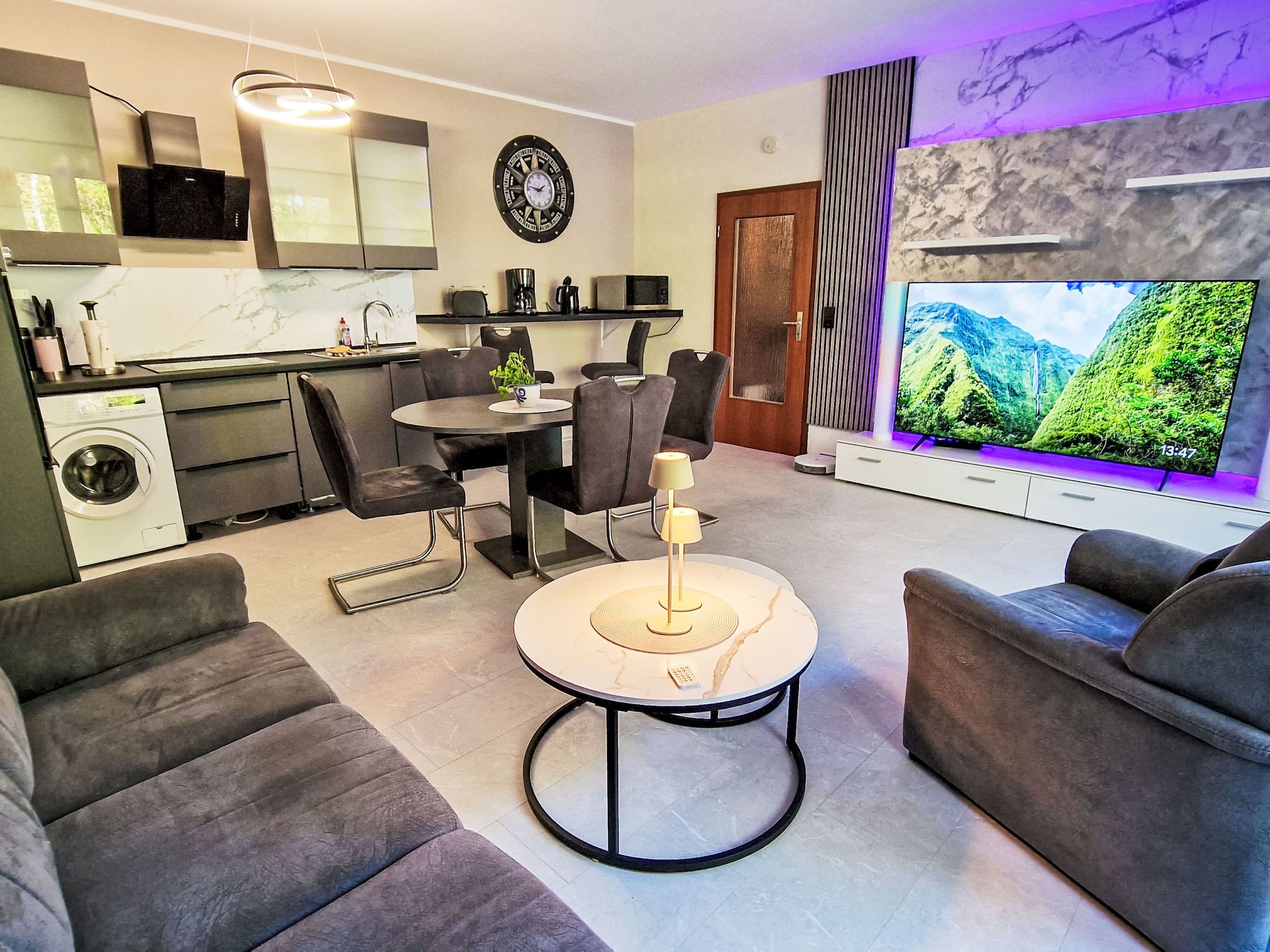 A modern living room with a dining area, a flat-screen TV, and a washing machine.