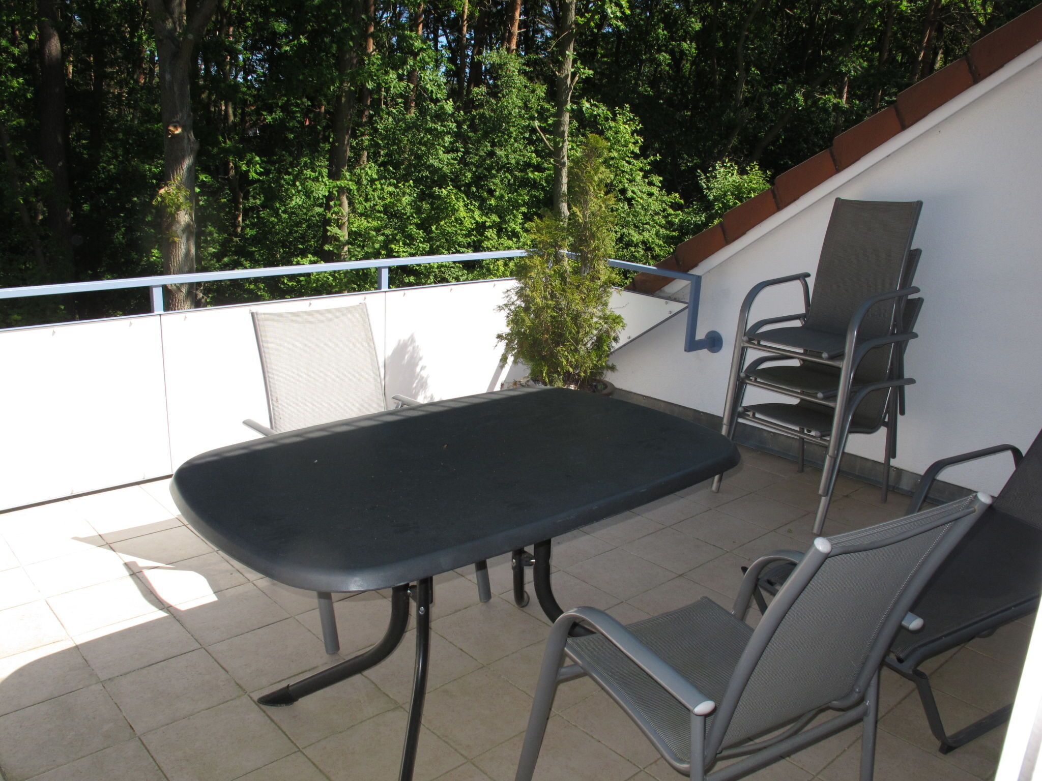 A balcony with a table and chairs, surrounded by a white wall and trees.