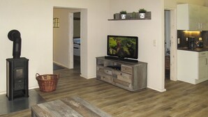 A living room with a TV, a fireplace, a wooden bench, and a kitchen area. - Apartment Helene by Interhome (Ribnitz-Damgarten)