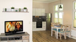 A compact kitchen with white cabinets, a stainless steel refrigerator, and a dining area with wooden chairs and a table. - Apartment Helene by Interhome (Ribnitz-Damgarten)