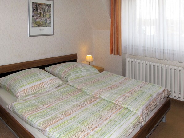 A hotel room with a double bed, a bedside lamp, a radiator, and a framed picture on the wall.