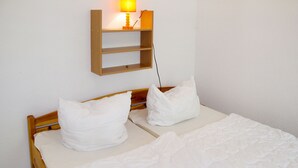 A neatly made bed with white bedding and pillows, a wooden headboard, and a wall-mounted shelf with a lamp. - Waldhäuser by Interhome (Himmelpfort)