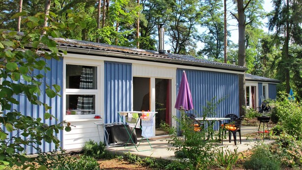 A small, single-story building with a blue exterior, a patio area with a table and chairs, and a barbecue grill. - Waldhäuser by Interhome (Himmelpfort)