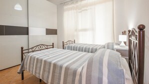 Et soveværelse med to senge, et natbord, en lampe og et stort vindue med gardiner.
