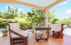 Relax in a serene outdoor setting surrounded by lush greenery and trees, with a table for two and comfortable seating.